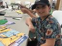 Boy wearing a Yankees cap sits at a table making a bead-and-pipe-cleaner craft