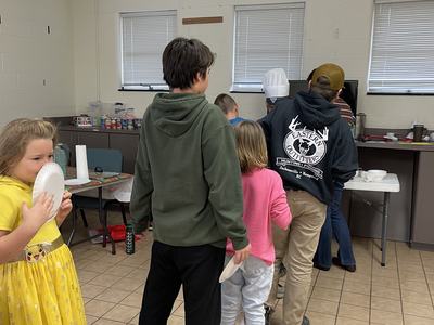 Group of children and teens standing in line at a serving table in a community room
