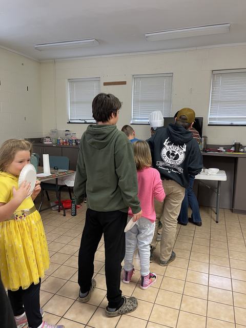 Group of children and teens standing in line at a serving table in a community room