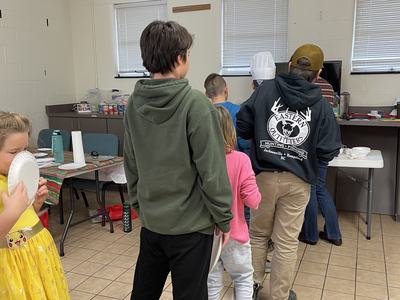Group of people lined up at a serving table in a community room; hoodie reads "Eastern Outfitters"
