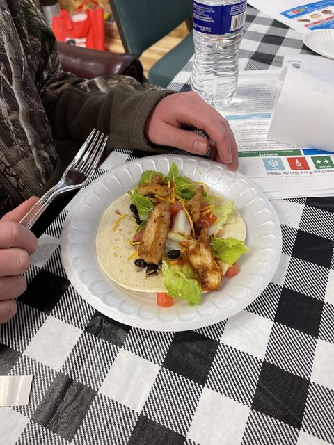 Person holding fork over chicken taco with lettuce, tomato, and black beans on paper plate