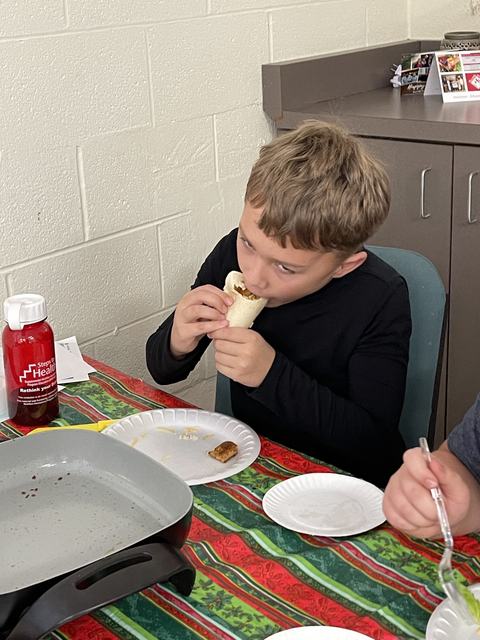 Boy eating a wrapped burrito at a table; red water bottle labeled "Steps to Health"