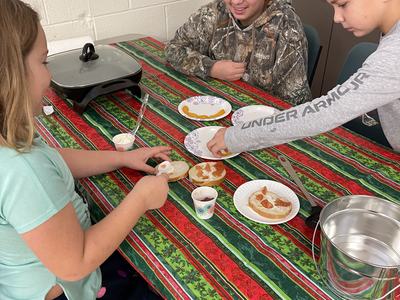 Three kids assembling bagels with cream cheese at a table; sleeve reads UNDER ARMOUR
