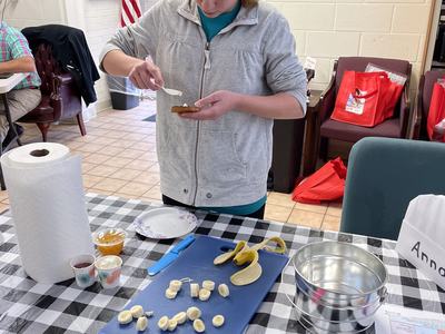 Person spreading topping on a toasted bun at a table with sliced bananas and utensils