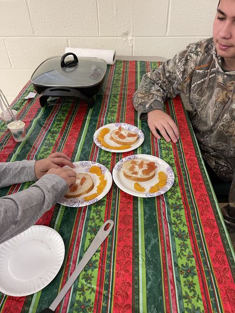 Two people assembling bagels with cream cheese and mandarin slices on holiday tablecloth