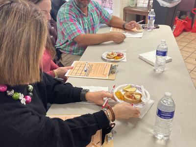 Three people seated at a table with clipboards, plates of snacks, and water bottles