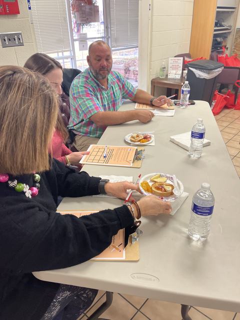 Three people seated at a table with clipboards, plates of snacks, and water bottles