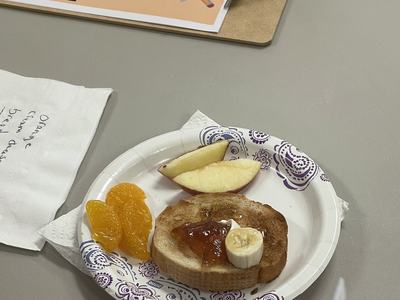 Paper plate with toast (jam, banana), apple and mandarin slices on table with clipboard "Judging Instructions"