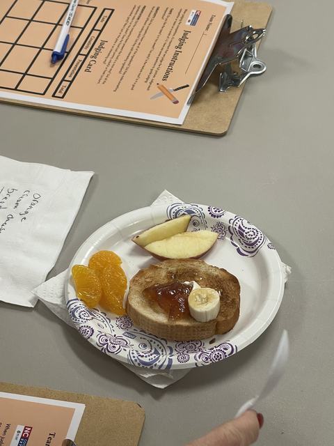 Paper plate with toast (jam, banana), apple and mandarin slices on table with clipboard "Judging Instructions"