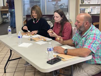 Three adults seated at a table eating snacks with bottled water in an office waiting area