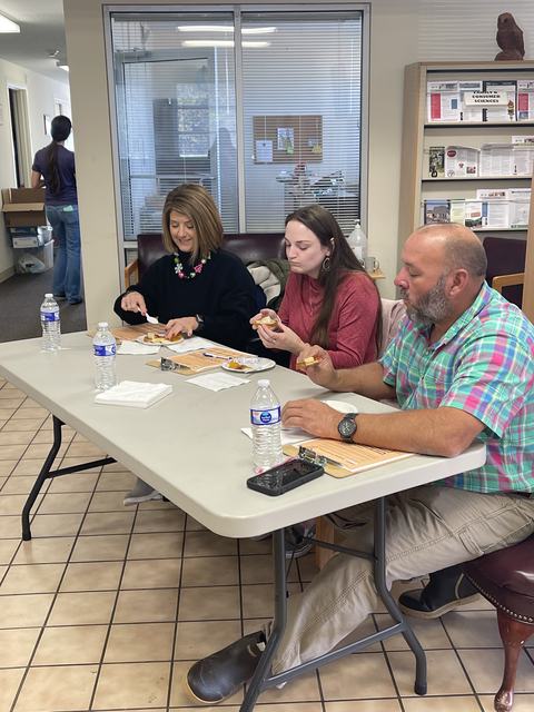 Three adults seated at a table eating snacks with bottled water in an office waiting area