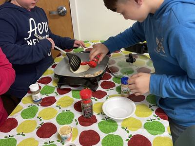 Two children at table seasoning and flipping food on an electric griddle