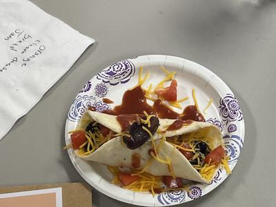 Paper plate with two soft tacos topped with shredded cheddar, diced tomatoes, black beans, and salsa