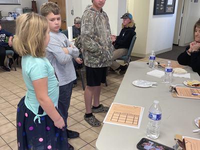 Three children standing by a table with clipboards and water bottles in a meeting room