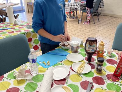 Boy in blue hoodie spooning dessert at table with banana slices and toppings