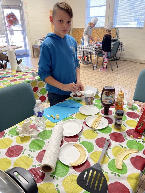 Boy in blue hoodie spooning dessert at table with banana slices and toppings