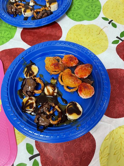 Blue plate with banana slices, pretzels, chocolate sauce and candied orange slices on table.