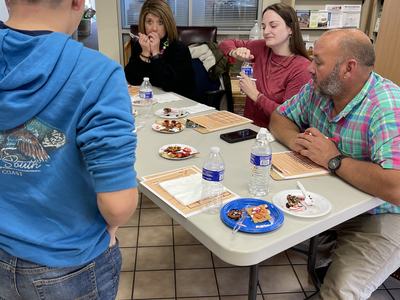 Four people seated at a table sampling snacks and bottled water while a boy stands nearby