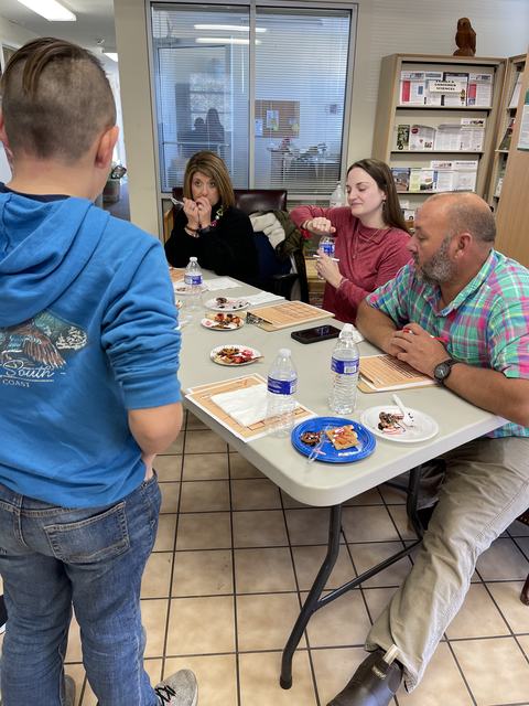 Four people seated at a table sampling snacks and bottled water while a boy stands nearby