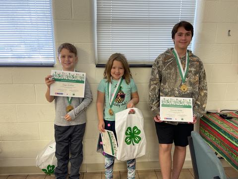 Three children standing with 4-H bags, medals, and Certificates of Achievement
