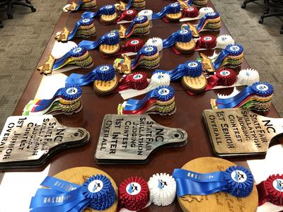 Table with rows of rosette ribbons and plaques labeled "NC State Fair Skillathon"