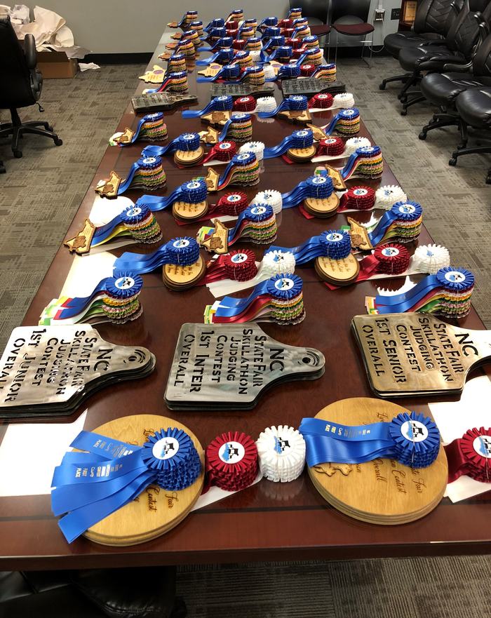 Table with rows of rosette ribbons and plaques labeled "NC State Fair Skillathon"