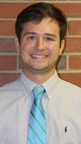 A man standing near a plain wall smiling.
