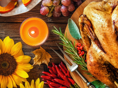 Roasted turkey on wooden platter surrounded by pumpkins, sunflowers, corn, grapes, and candle