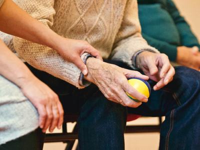 Caregiver holding elderly person's forearm while they hold a yellow stress ball.
