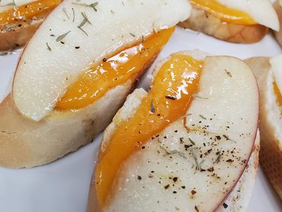 Baguette slices topped with melted cheddar, thin apple slices, and dried herbs