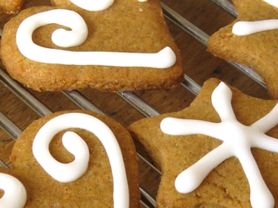 Gingerbread cookies on a cooling rack being decorated with white icing swirls