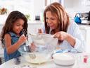Woman and girl baking: woman sifting flour as girl whisks batter