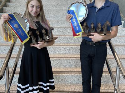 Two youths standing on stairs holding horse-head trophies and blue-yellow ribbons