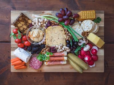 Charcuterie board with cheeses, crackers, grapes, meats, nuts, pickles, and vegetables