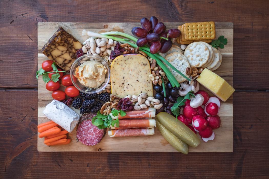 Charcuterie board with cheeses, crackers, grapes, meats, nuts, pickles, and vegetables