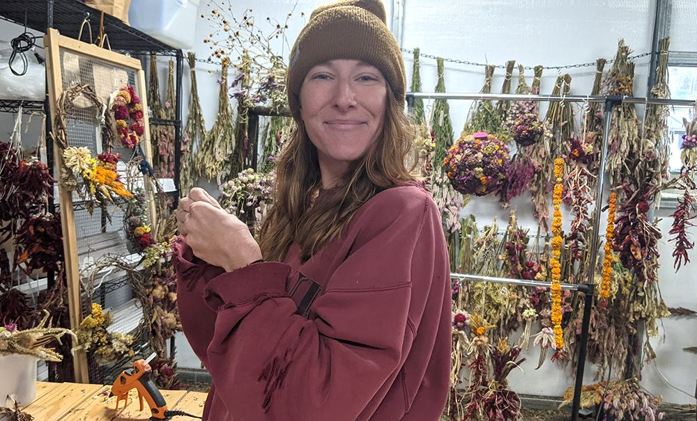 Woman wearing a beanie arranging dried flowers and hanging wreaths in a workshop