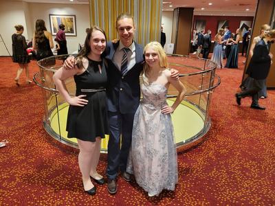 Three young people in formal attire posing with arms around each other in a hotel lobby