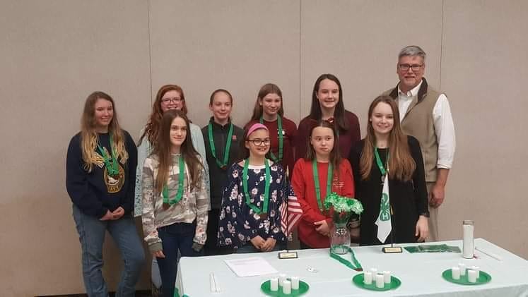 Group of girls with green medals and an adult standing behind a table with candles