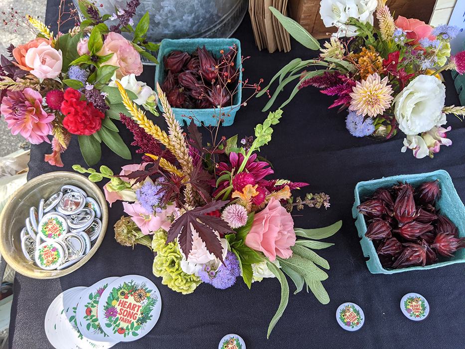Colorful floral bouquets, baskets of dark red roselle pods, stickers reading "HEART SONG FARM"