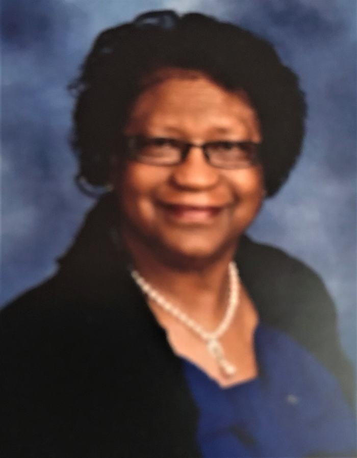 Head-and-shoulders portrait of a woman wearing glasses, a pearl necklace, and a blue top