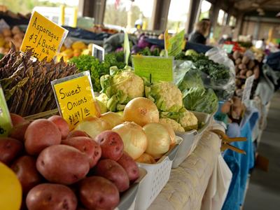 Farmers market display of potatoes, onions, cauliflower with sign "Sweet Onions $1.49/lb"