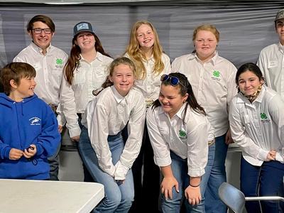 Group of youth and adults wearing white 4‑H shirts posing indoors