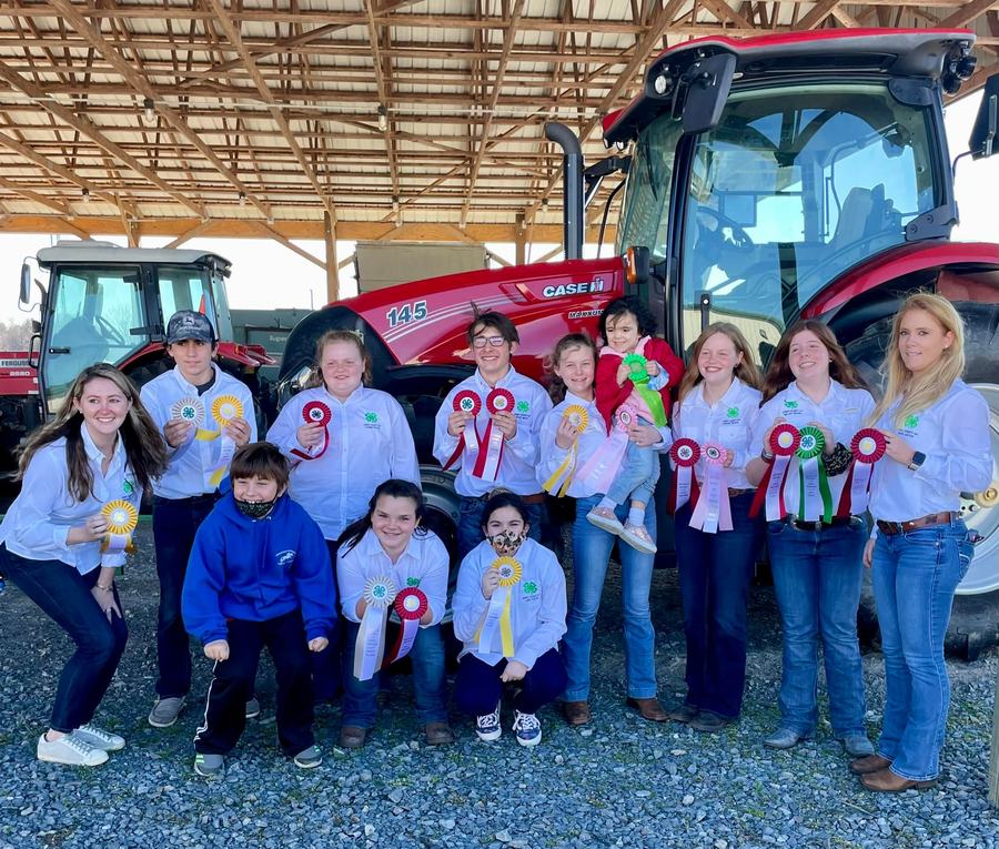 Group of 4-H members holding award ribbons in front of a red Case IH 145 tractor