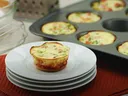 Mini egg-and-vegetable frittata on stacked white plates, muffin tin with frittatas behind