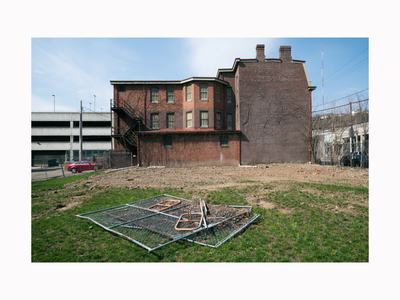 Three-story brick building with exterior fire escape and collapsed chain-link fence on vacant lot