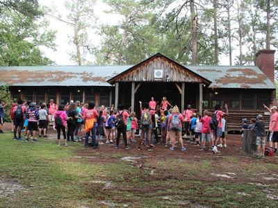Group of children and staff gathered outside rustic camp lodge in wooded area