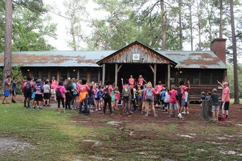 Group of children and staff gathered outside rustic camp lodge in wooded area