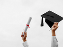 Hands holding a rolled diploma and a mortarboard graduation cap against a white sky