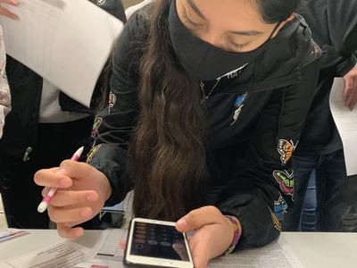 Person wearing mask uses phone and pen to fill forms over papers titled "Housing Book"