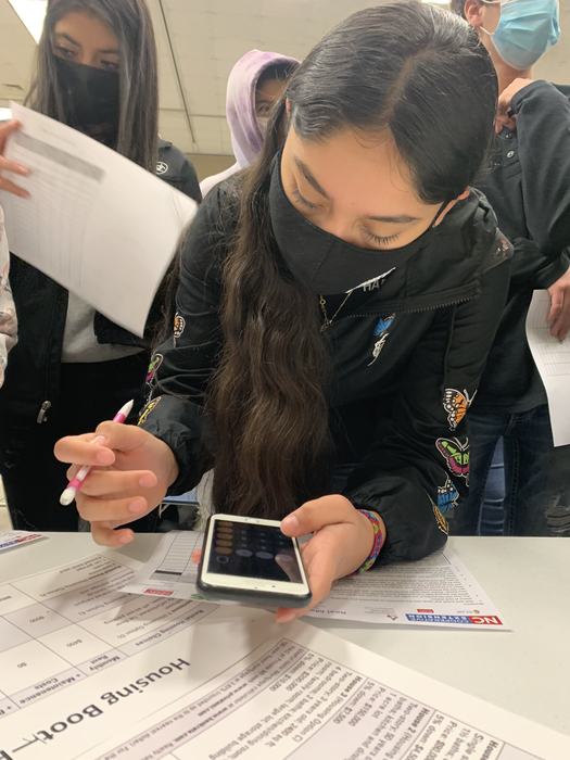 A girl doing a workbook using her phone's calculator.